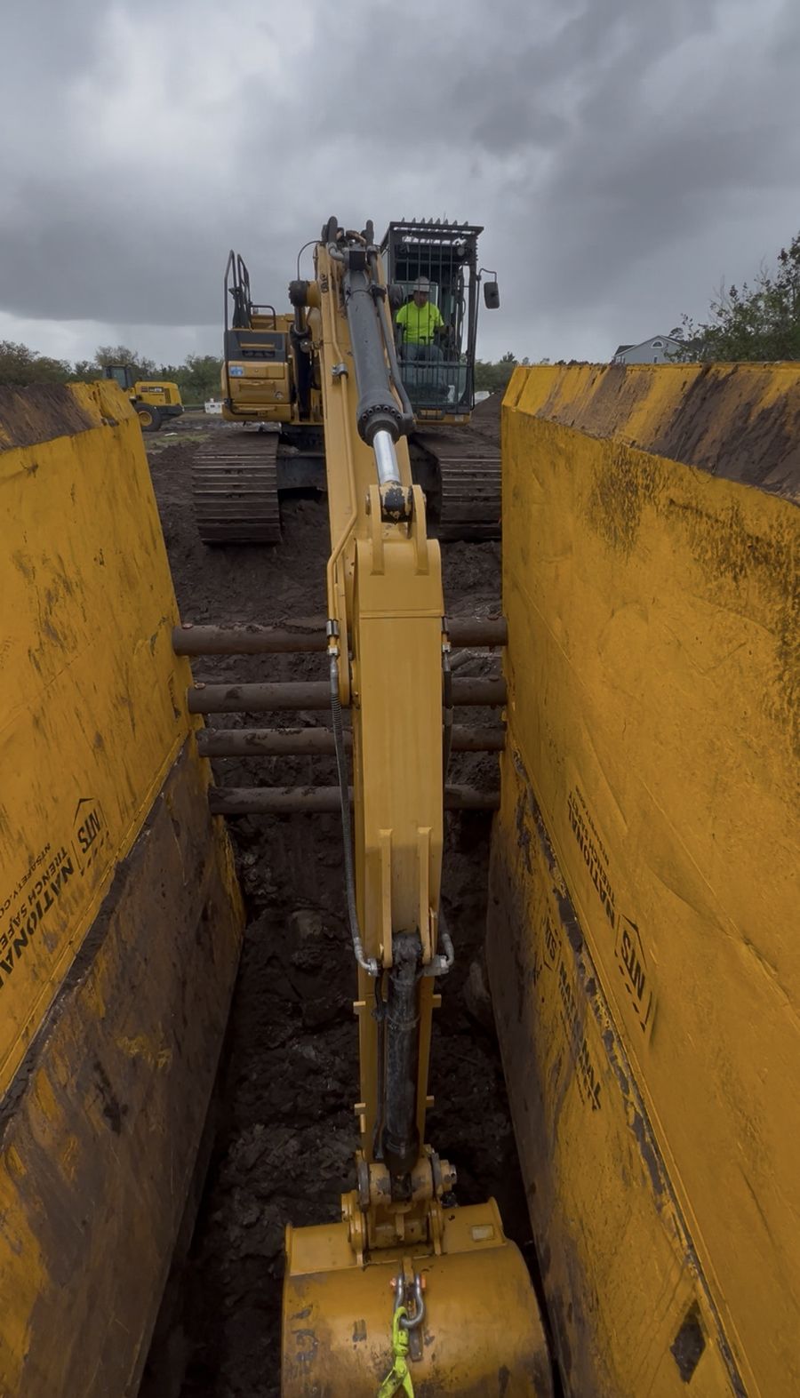Excavator working a shored trench under trench boxes on a Central Florida site